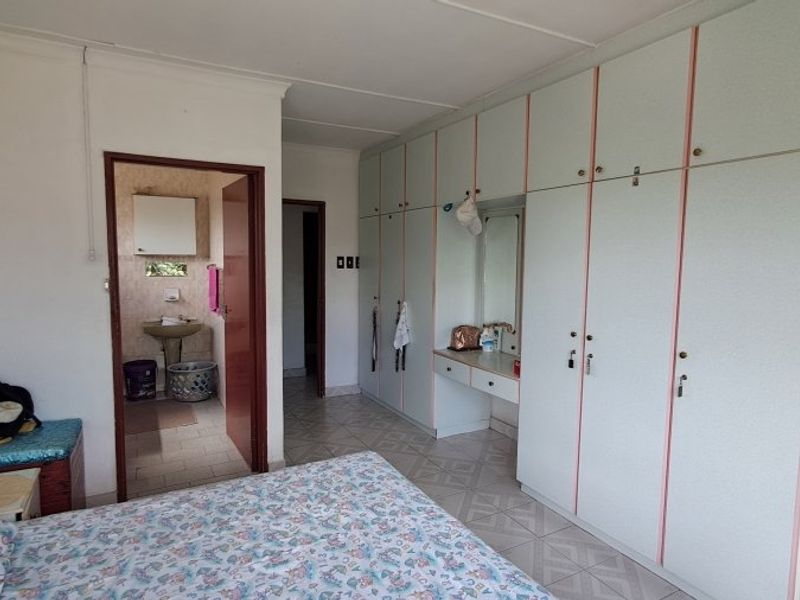 Bedroom featuring extensive built-in cupboards with integrated vanity and an adjoining en-suite bathroom, showcasing dated finishes throughout.