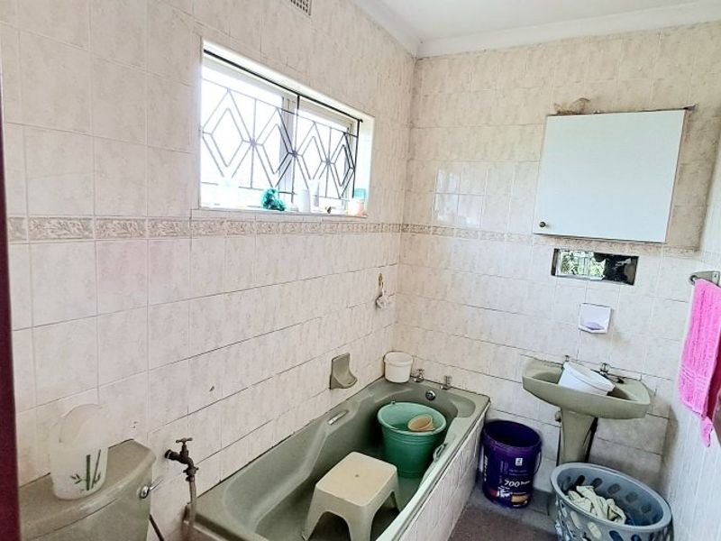 A dated bathroom featuring a bathtub, pedestal basin, and full-height wall tiling, requiring modernization to improve functionality and aesthetic appeal.