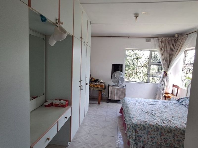 A functional bedroom featuring extensive built-in cupboards with an integrated vanity, tiled flooring, and security bars on the windows.