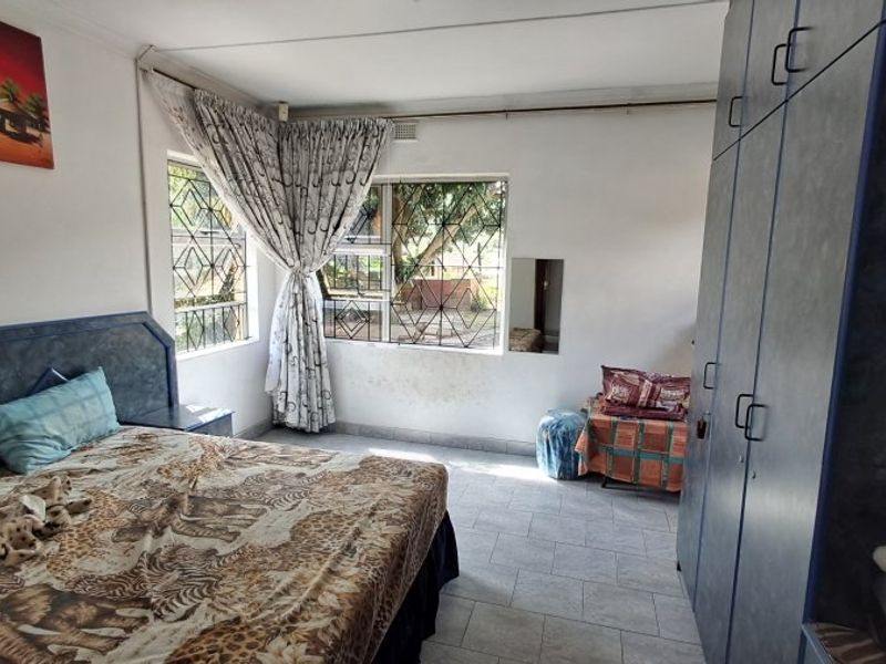 A bedroom featuring tiled flooring, built-in cupboards, and security bars on the windows, requiring cosmetic updates to the wall finishes.