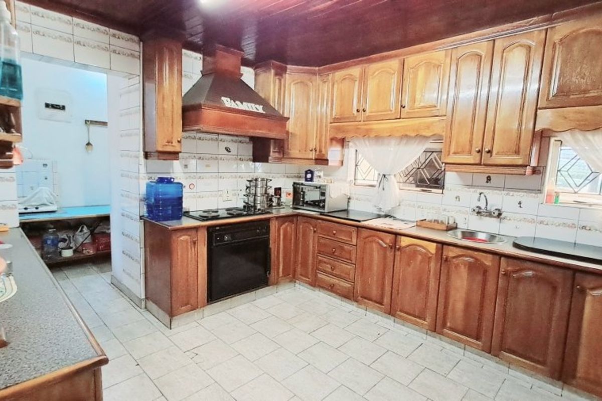 A traditional kitchen featuring extensive wooden cabinetry, built-in oven, hob, extractor fan, and tiled splashbacks with a timber ceiling finish.