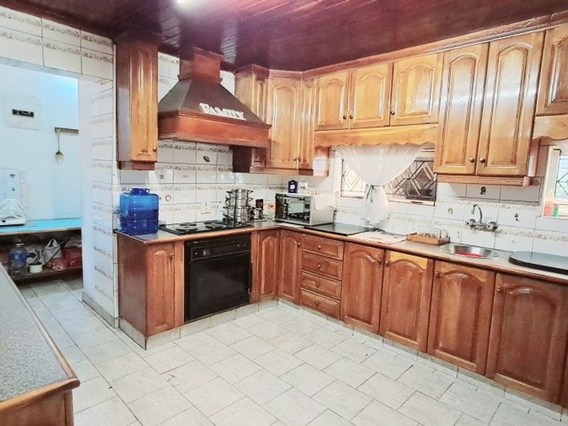 A traditional kitchen featuring extensive wooden cabinetry, built-in oven, hob, extractor fan, and tiled splashbacks with a timber ceiling finish.
