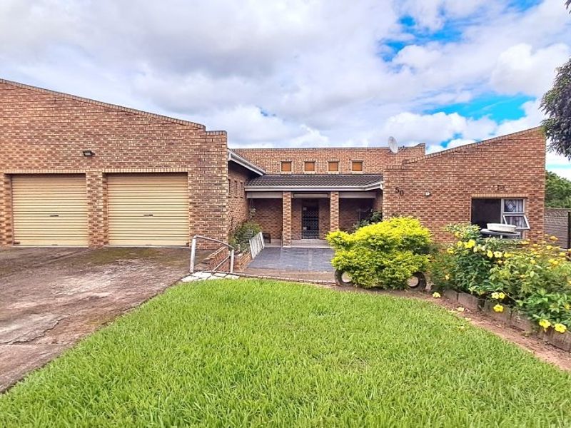 Front view of a brick house featuring a double garage, paved driveway, and a covered entrance area with established garden beds.