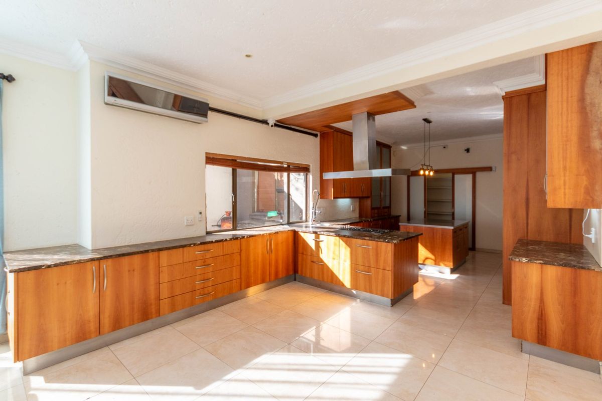 Spacious kitchen featuring warm-toned wooden cabinetry, stone countertops, integrated stainless steel extractor fan, and tiled flooring in an open-plan layout.