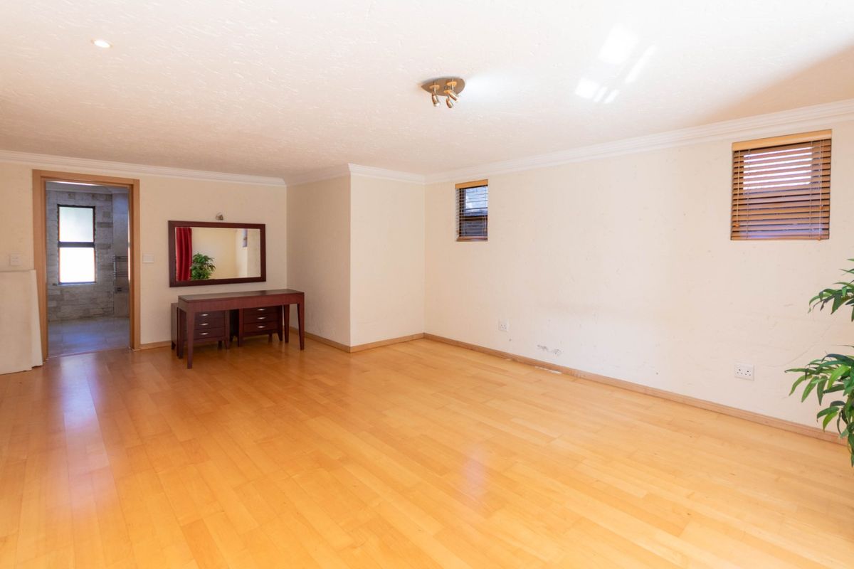 A spacious, light-filled bedroom featuring laminate flooring, coved cornicing, and dual windows with fitted venetian blinds.