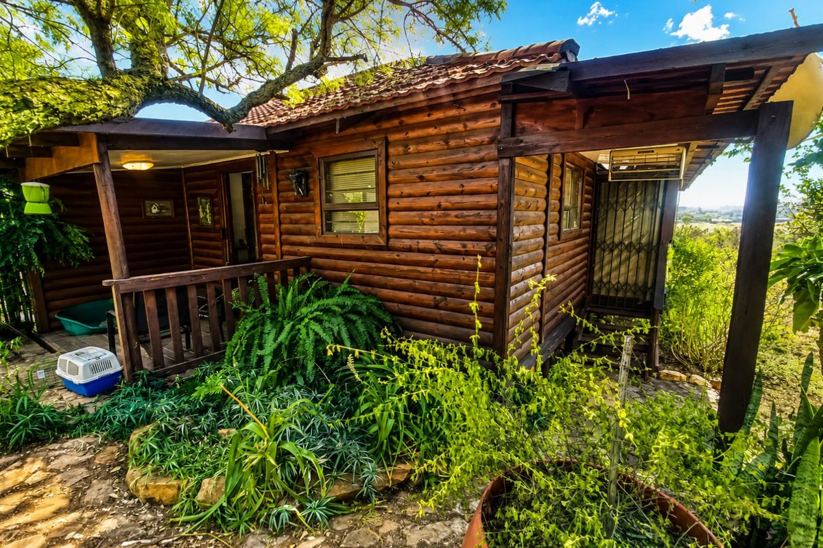 A rustic log cabin exterior featuring a covered patio area, timber construction, and established garden surroundings.