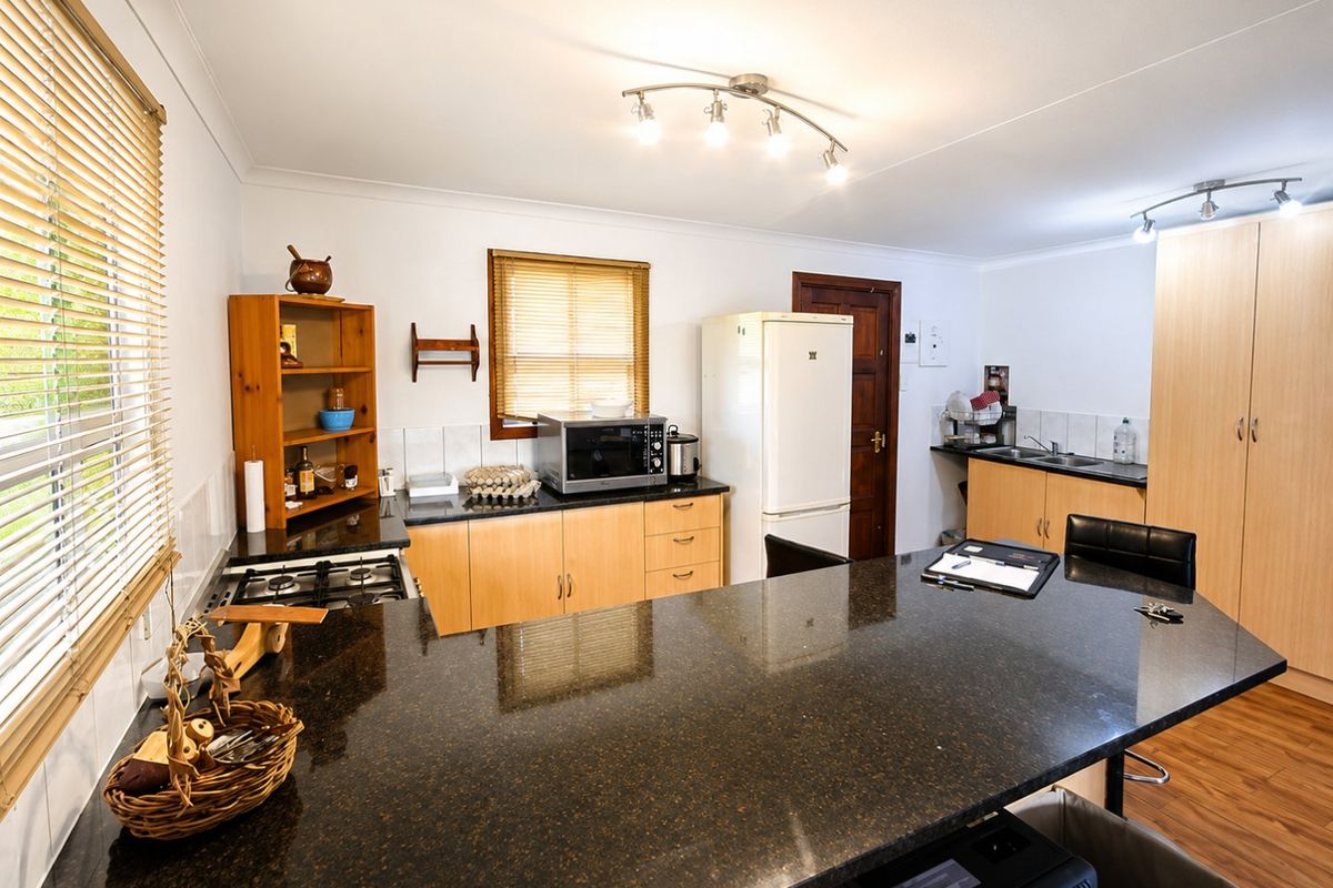 A functional kitchen featuring dark granite countertops, light wood cabinetry, a gas hob, and a breakfast bar island with laminate flooring.
