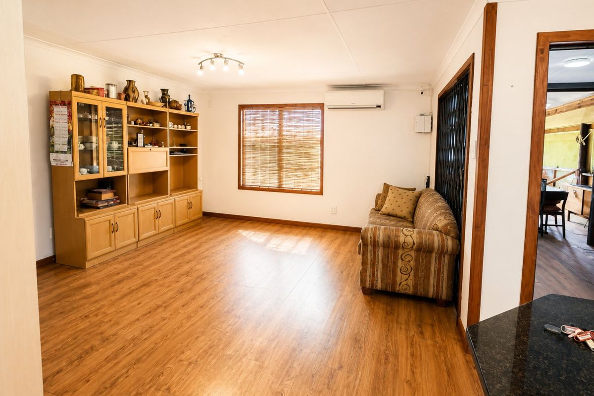A well-lit living room featuring laminate flooring, a wall-mounted split-system air conditioner, and a security gate leading to an adjacent space.