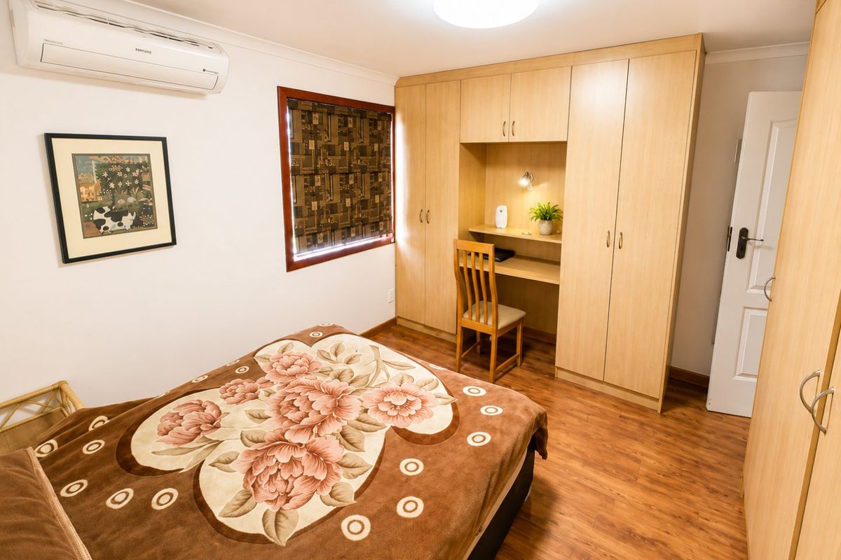 A well-maintained bedroom featuring built-in cabinetry with an integrated desk, laminate flooring, and a wall-mounted split-system air conditioner.
