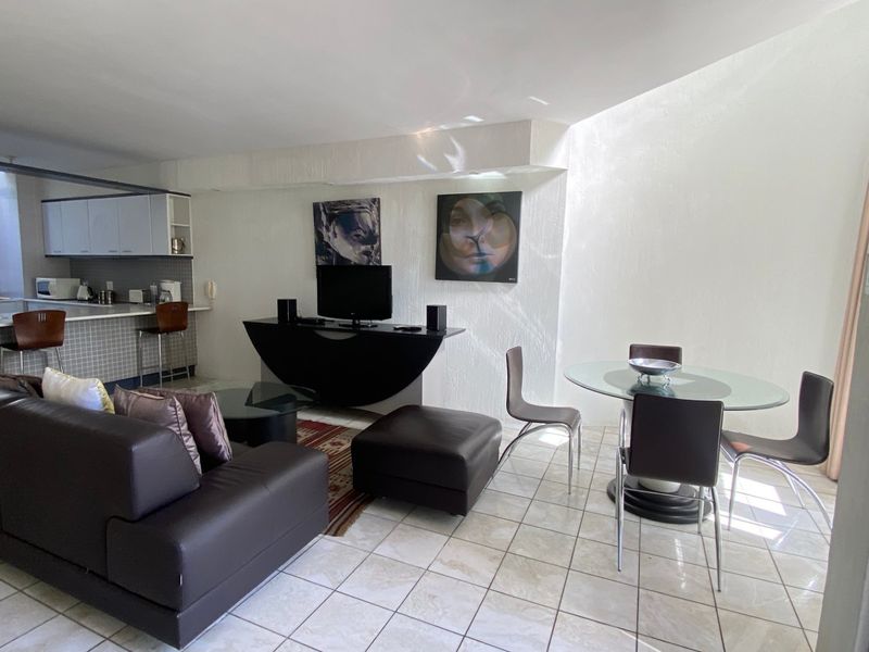 An open-plan living, dining, and kitchen area featuring tiled flooring and a breakfast bar, offering a functional layout for modern apartment living.