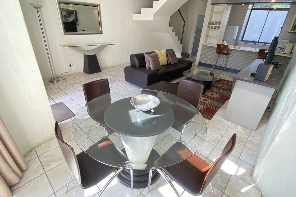 Open-plan living and dining area featuring tiled flooring, a staircase, and an integrated kitchen with a breakfast bar.