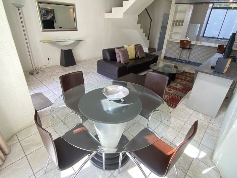 Open-plan living and dining area featuring tiled flooring, a staircase, and an integrated kitchen with a breakfast bar.