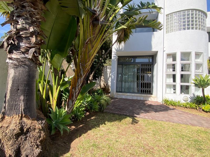 Rear exterior view of the apartment featuring a brick paved patio, landscaped garden, and a secure sliding door entrance.