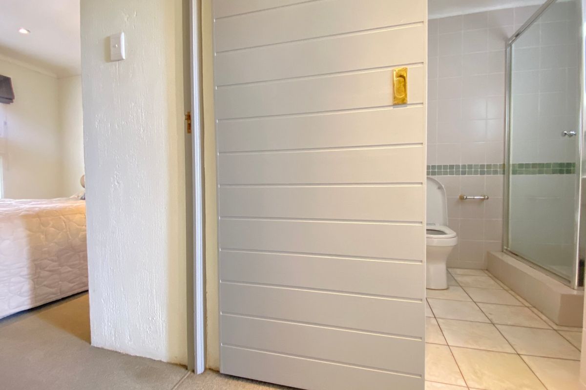 A bathroom featuring tiled walls and flooring, a shower enclosure, and a toilet, accessed via a sliding door from the adjacent bedroom.