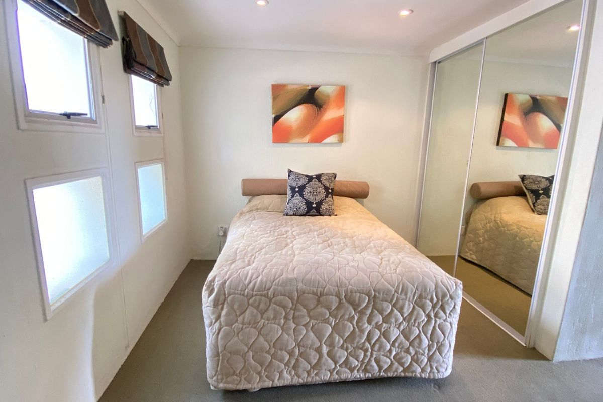 A compact bedroom featuring neutral walls, carpeted flooring, recessed downlighting, and a large mirrored sliding wardrobe for storage.