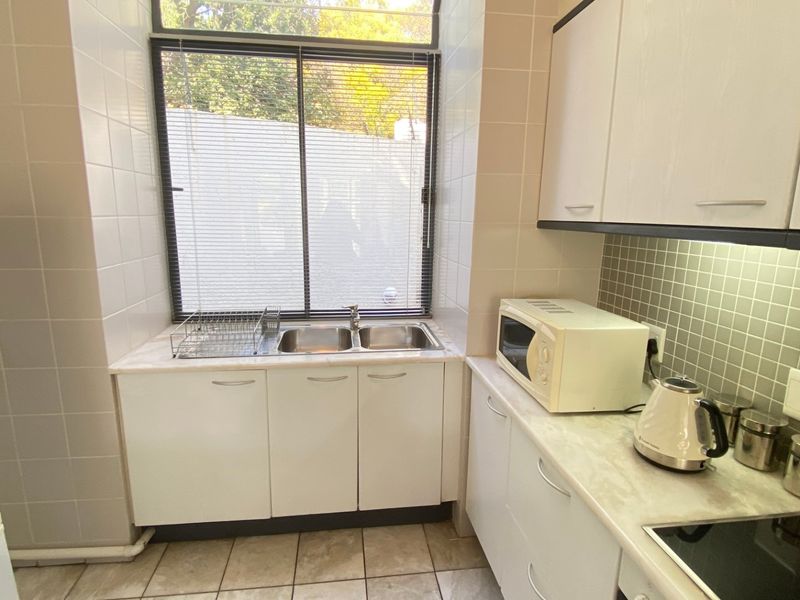 A functional kitchen featuring white cabinetry, laminate countertops, a double basin sink, and tiled backsplash with integrated electric hob.
