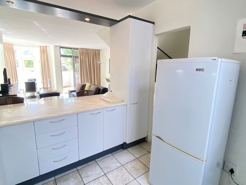 Open-plan kitchen and living area featuring white cabinetry, stone countertops, tiled flooring, and direct access to an outdoor patio space.