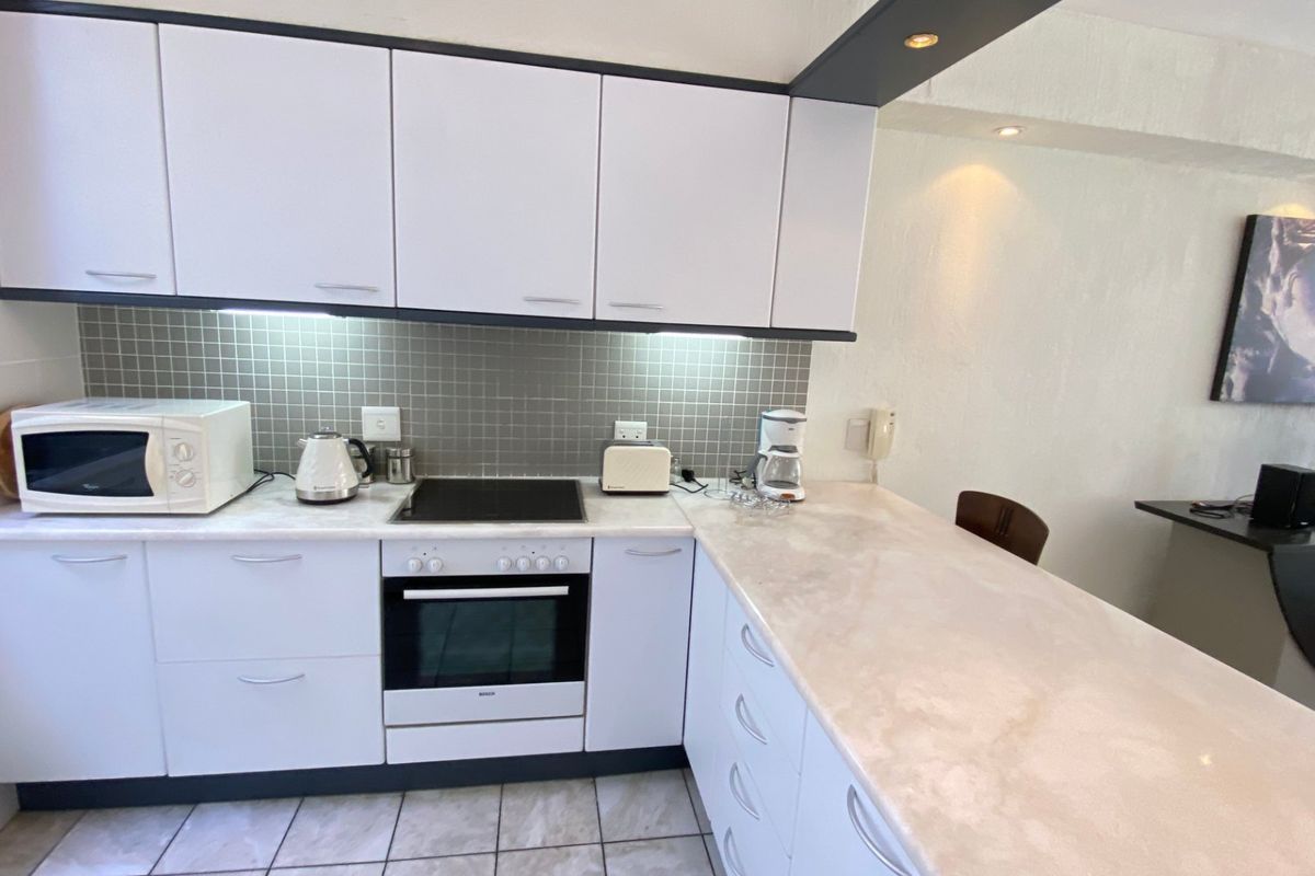 A functional kitchen featuring white cabinetry, stone countertops, a tiled backsplash, and integrated appliances including an electric hob and oven.
