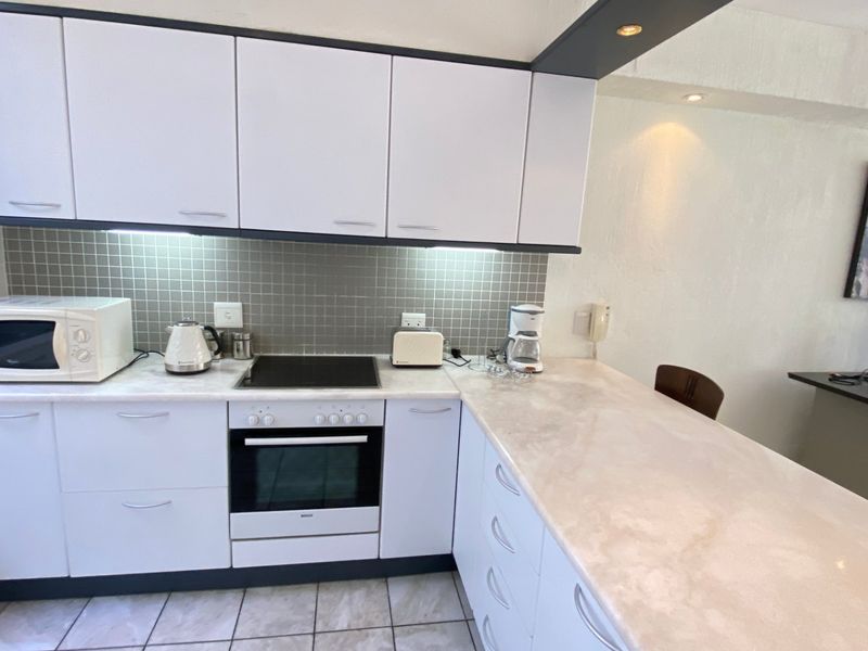 A functional kitchen featuring white cabinetry, stone countertops, a tiled backsplash, and integrated appliances including an electric hob and oven.
