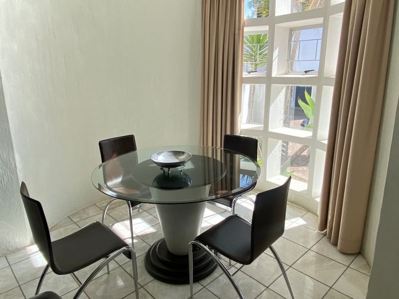 A bright dining area featuring tiled flooring and a large, curved grid-pattern window that allows for ample natural light.
