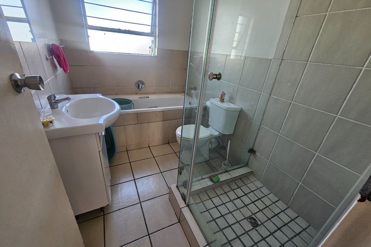 A functional bathroom featuring a pedestal basin, built-in bathtub, and a separate glass-enclosed shower with tiled finishes throughout.