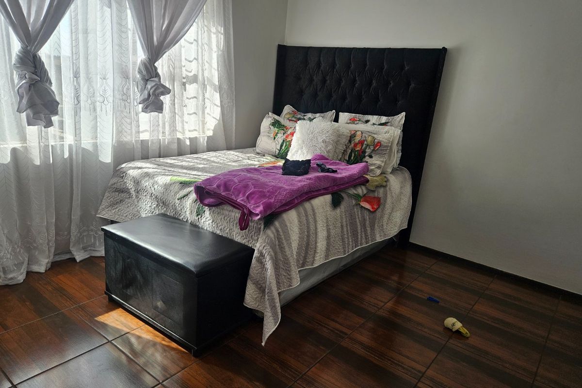 A bedroom featuring dark wood-look tiled flooring and natural light from a window with installed curtain rails.