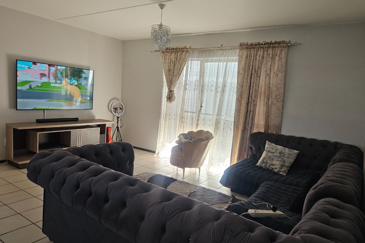 A living room featuring tiled flooring and a sliding glass door with curtains, providing natural light to the space.