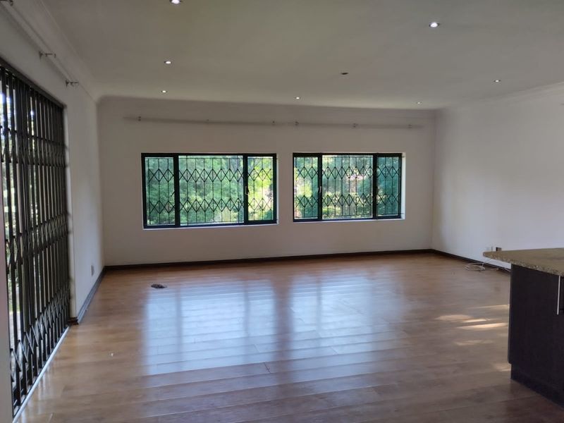 Spacious open-plan living area featuring laminate flooring, recessed lighting, and large windows with security gates, offering a bright and versatile layout.