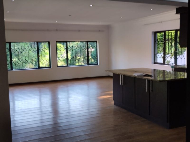 Spacious open-plan living area featuring laminate flooring, recessed lighting, and a modern kitchen island with granite countertops and dark cabinetry.