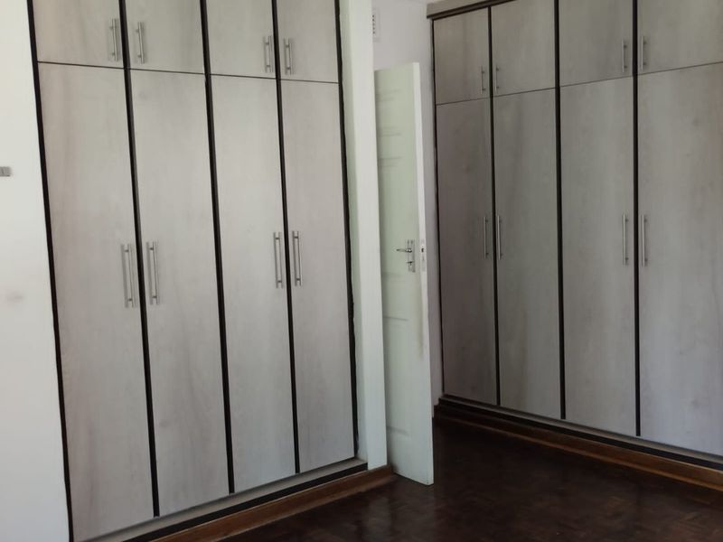 Bedroom featuring extensive built-in cupboards with light wood-grain finish and dark parquet flooring.