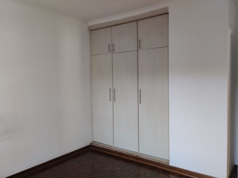 A clean, empty bedroom featuring light-toned built-in cupboards and dark parquet flooring, offering a neutral space ready for personalization.