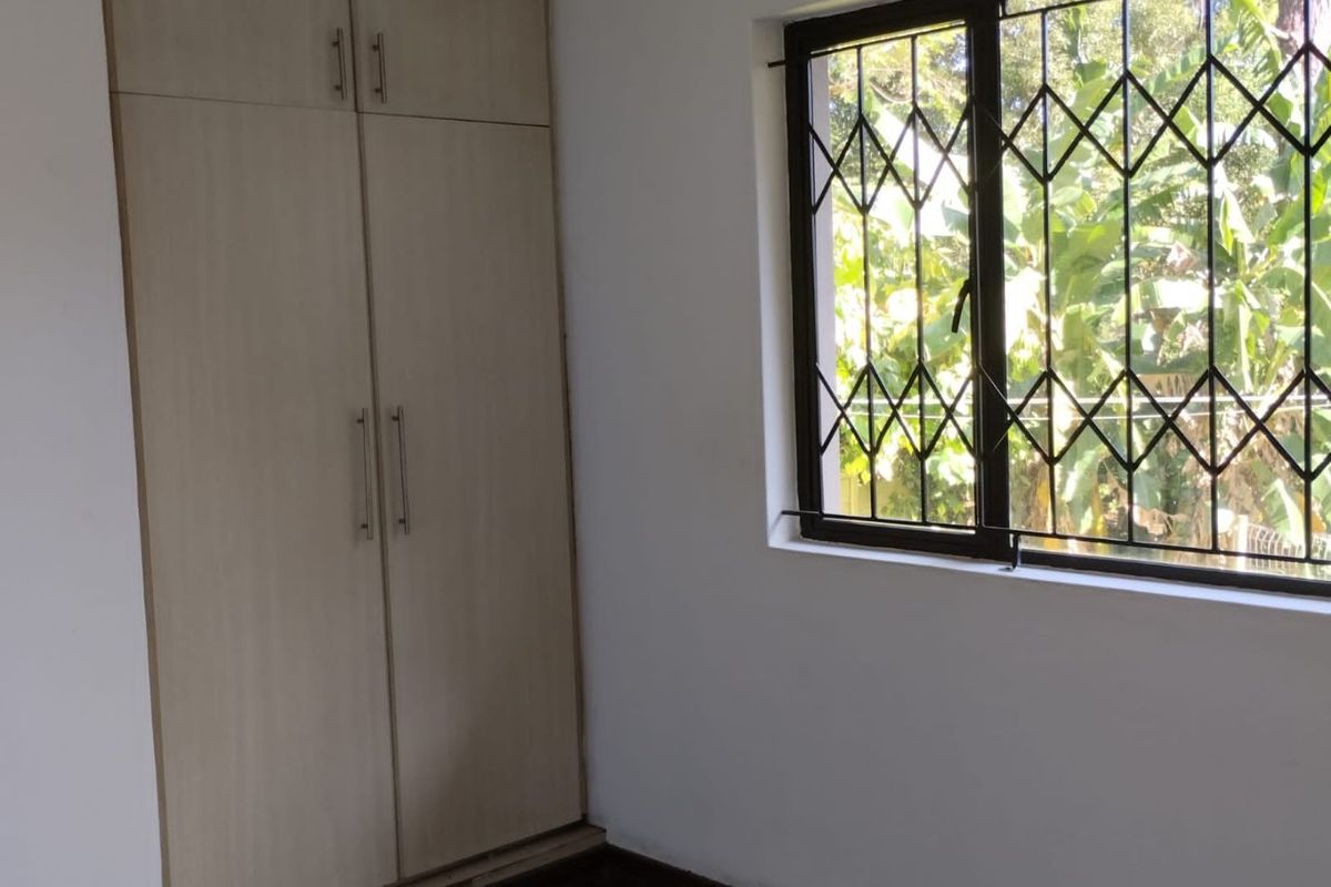 A bright, empty bedroom featuring neutral built-in cupboards and a window fitted with security bars.