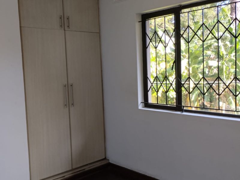 A bright, empty bedroom featuring neutral built-in cupboards and a window fitted with security bars.