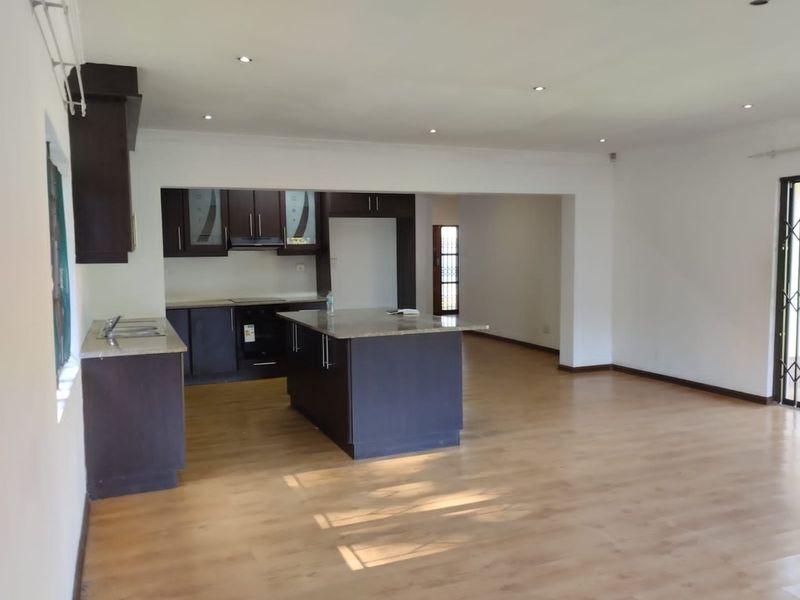 Spacious open-plan living area featuring a modern kitchen with dark cabinetry, granite countertops, a central island, and laminate flooring throughout.