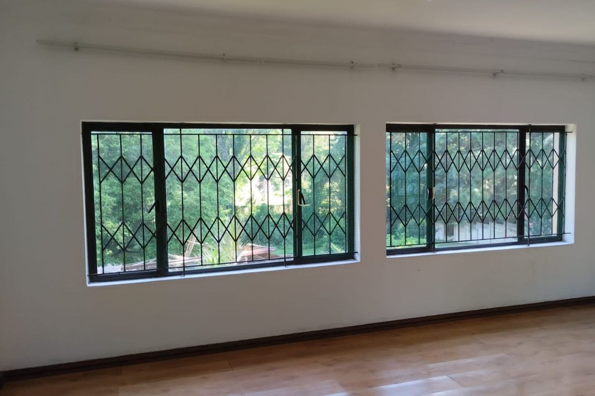 A bright, empty living area featuring laminate flooring, recessed downlights, and large windows fitted with security gates.