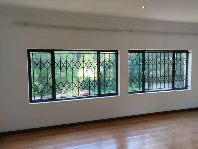 A bright, empty living area featuring laminate flooring, recessed downlights, and large windows fitted with security gates.