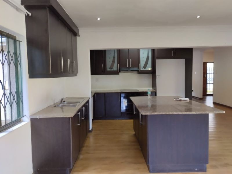 Modern kitchen featuring dark wood cabinetry, stone countertops, a central island, and built-in appliances, offering a clean and functional workspace.