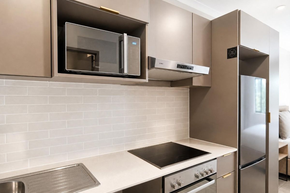 Modern kitchen featuring sleek taupe cabinetry, subway tile backsplash, brass fixtures, and high-quality built-in appliances including an induction cooktop and oven.