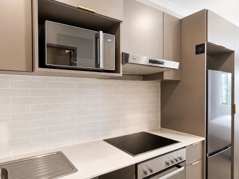 Modern kitchen featuring sleek taupe cabinetry, subway tile backsplash, brass fixtures, and high-quality built-in appliances including an induction cooktop and oven.