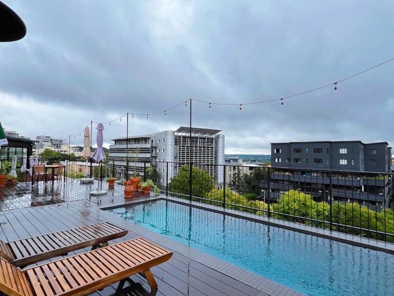 Elevated apartment pool area featuring timber decking, a modern swimming pool, and metal balustrades with expansive urban views.