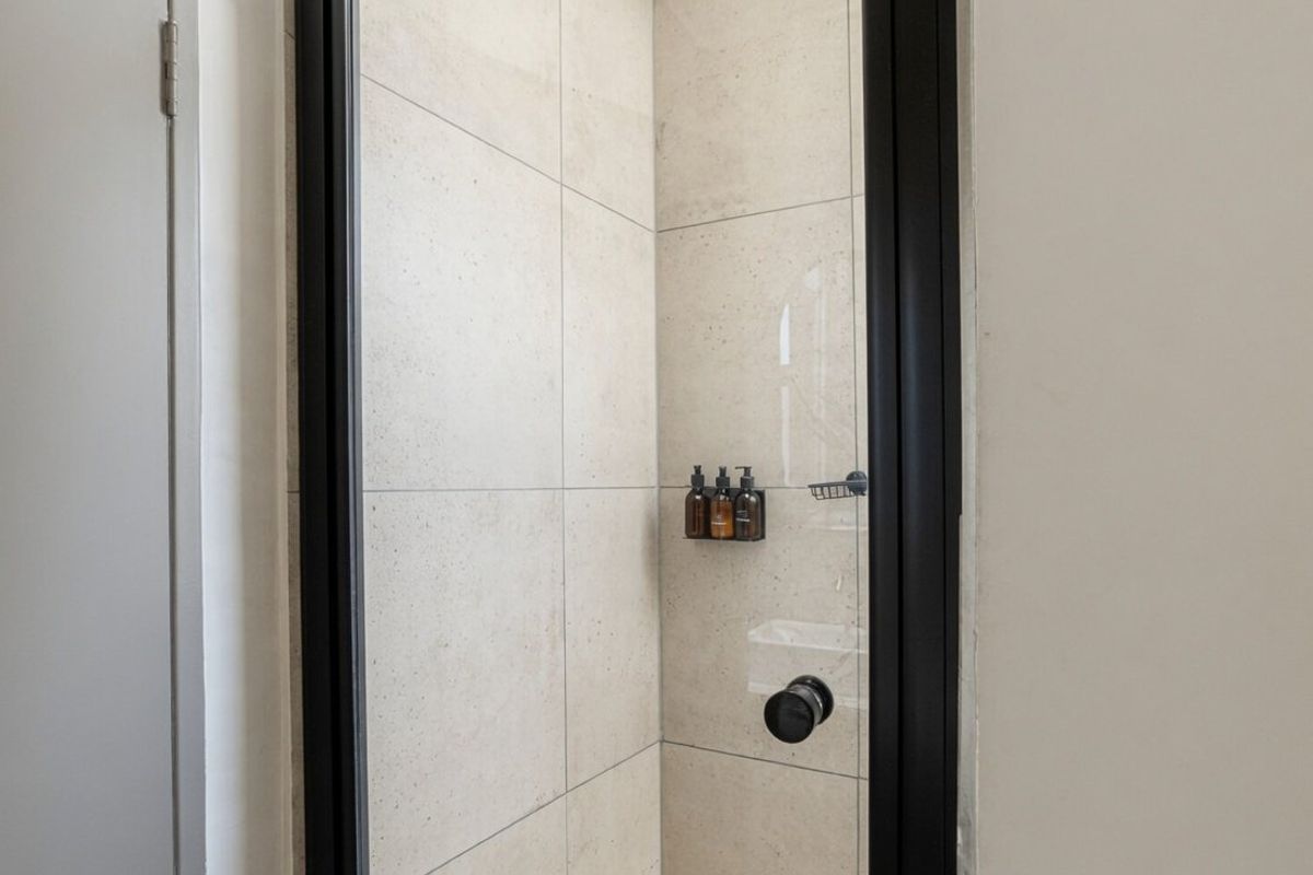 A modern shower enclosure featuring large format neutral tiles and a sleek black metal frame.