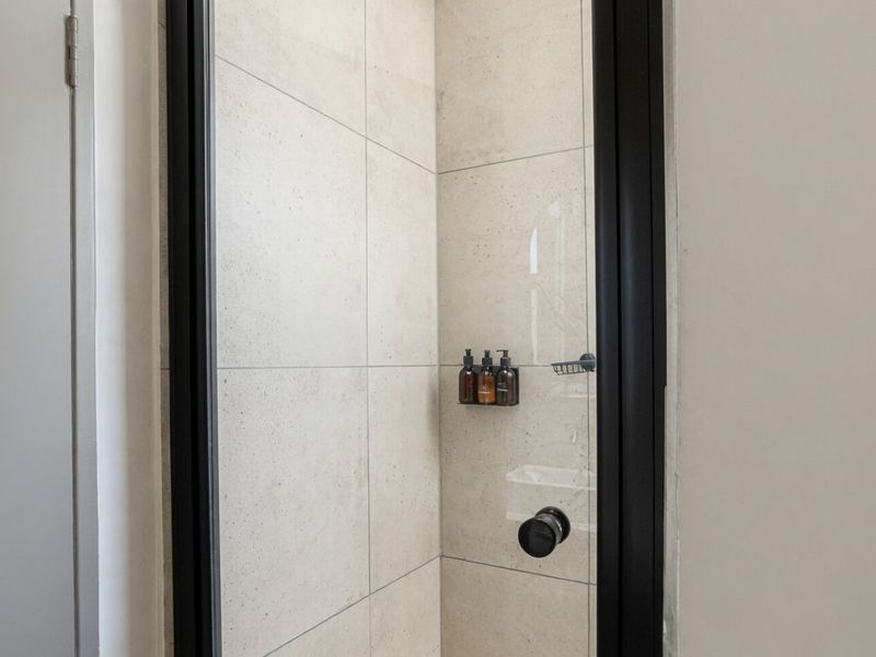 A modern shower enclosure featuring large format neutral tiles and a sleek black metal frame.