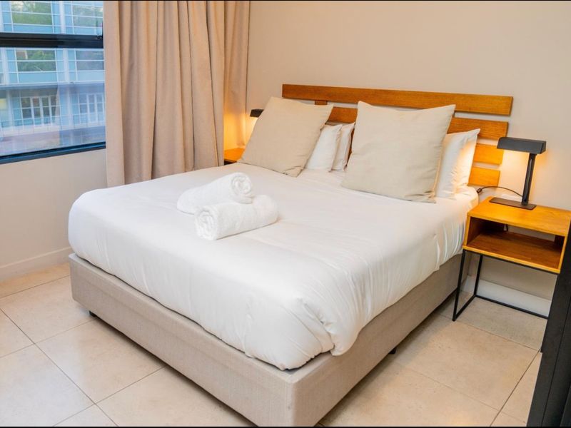 A well-maintained bedroom featuring neutral tiled flooring and a large window, providing a clean and comfortable living space.