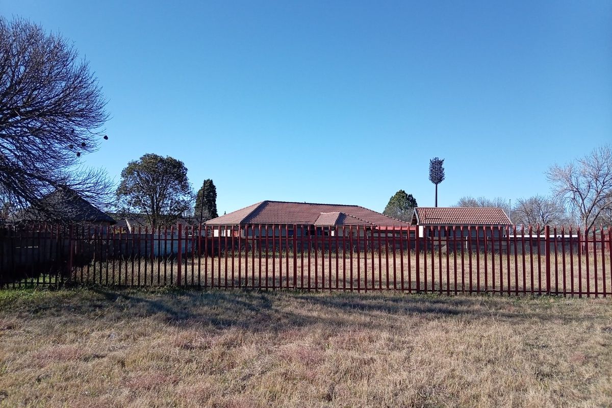 A view of the rear of the property featuring a tiled roof house enclosed by steel palisade fencing and an open grass area.