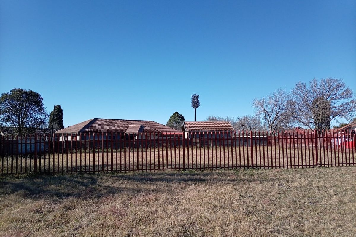 A view of the rear of the property featuring a tiled roof structure enclosed by a steel palisade fence.