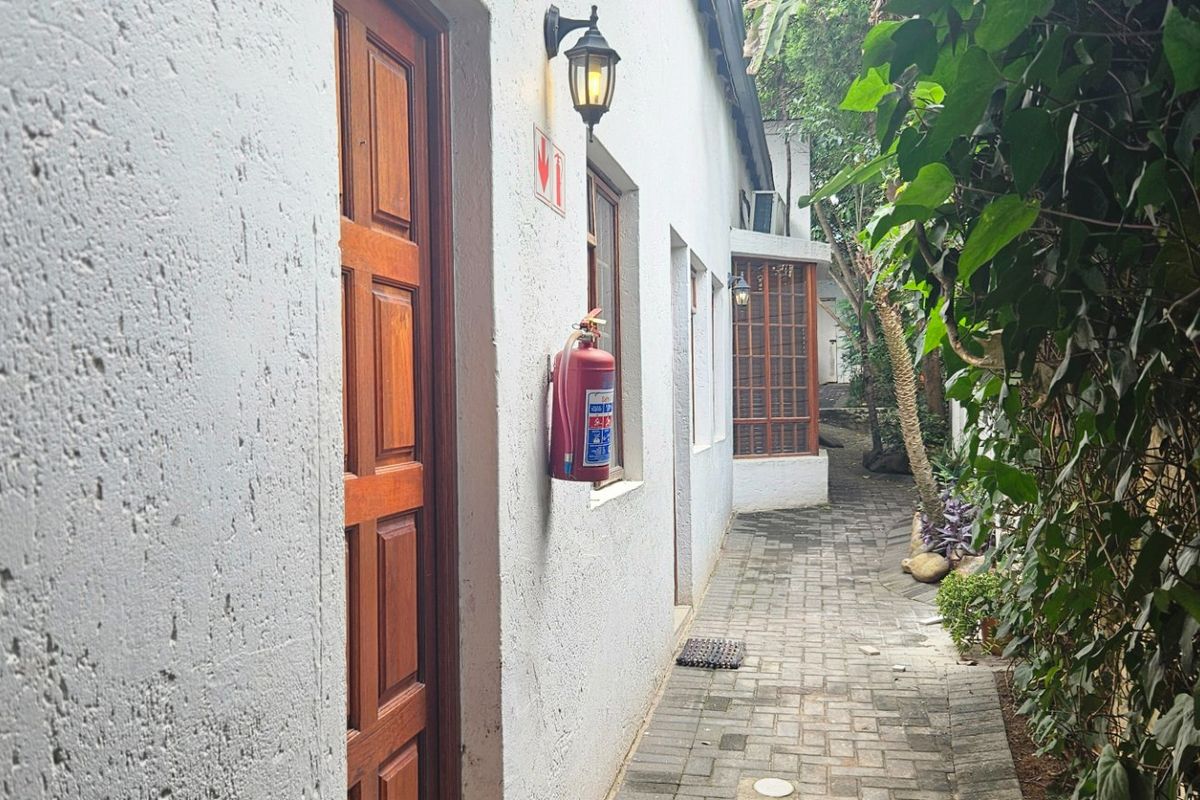 A narrow paved side walkway along the exterior of the building, featuring timber doors, windows, and wall-mounted lighting.