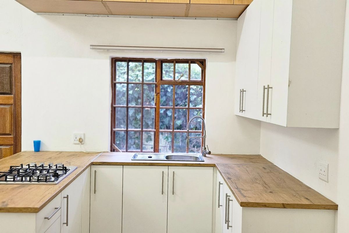 A functional kitchen featuring white cabinetry, wood-look countertops, a gas hob, and a stainless steel sink, set against a classic timber-framed window.