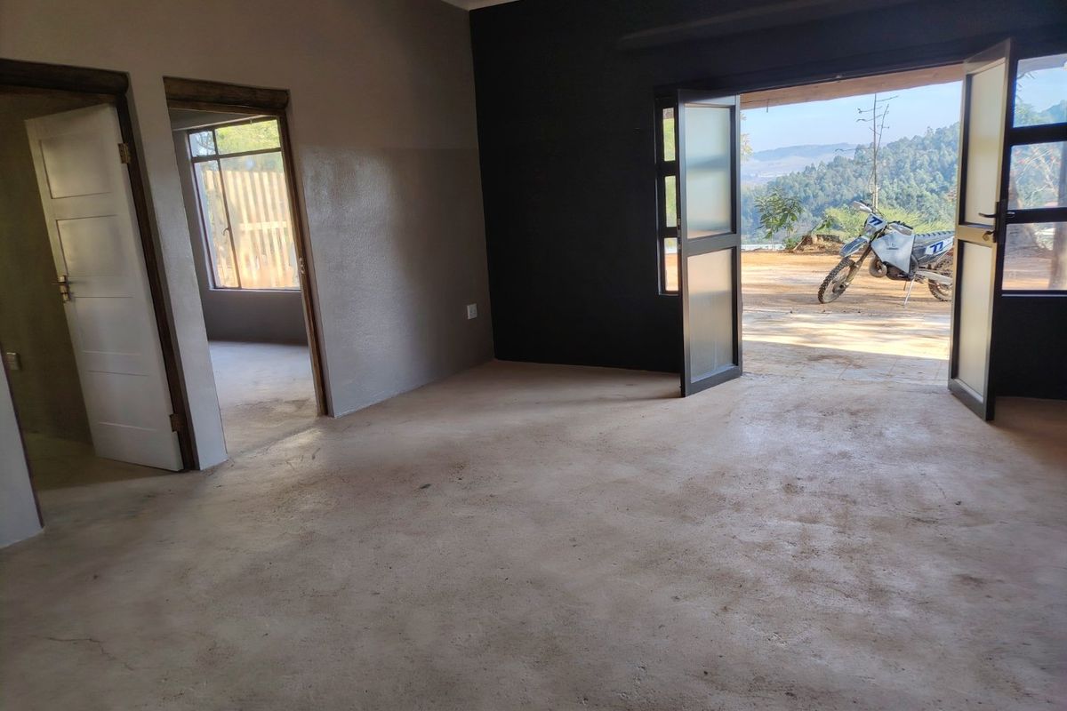 An empty living area featuring concrete flooring and double doors opening to an outdoor view, providing a blank canvas for interior design.