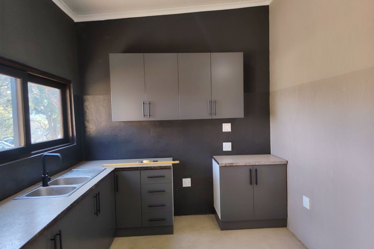 A modern, minimalist kitchen area featuring dark grey cabinetry, laminate countertops, a double bowl sink, and neutral wall finishes.