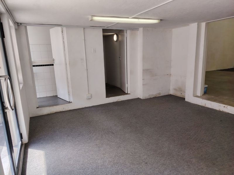 An empty utility or office space featuring carpeted flooring, fluorescent lighting, and access to a small tiled secondary area.